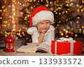 child in Santa Claus hat on Christmas tree background with gift and book  133933572