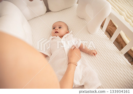 A mother gently interacts with her baby in a crib A mother gently interacts with her baby in a crib 133934161