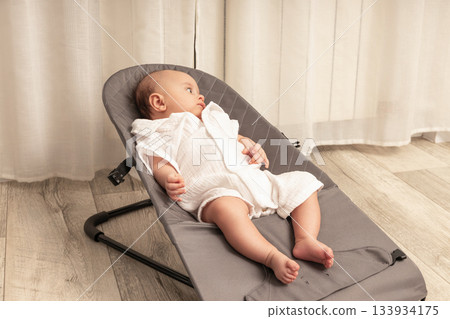 Baby enjoys a peaceful moment in a cozy bouncer at home Baby enjoys a peaceful moment in a cozy bouncer at home 133934175