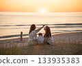 Back view of two caucasian female friends and a child enjoying sunset on the Baltic seashore.  133935383