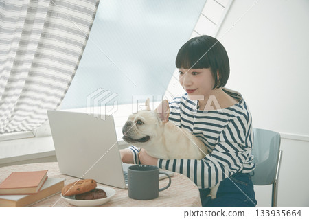 一名女子正在使用電腦，旁邊還有一隻狗。 133935664