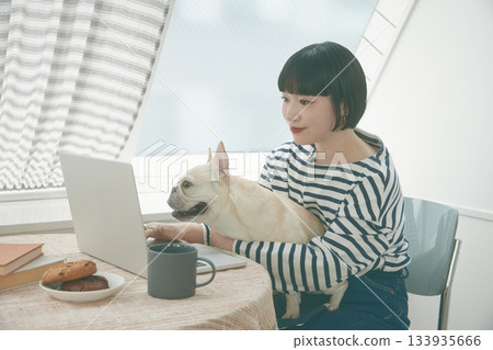 一名女子正在使用電腦，旁邊還有一隻狗。 133935666