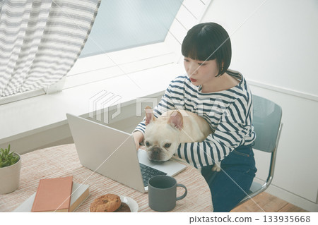 一名女子正在使用電腦，旁邊還有一隻狗。 133935668
