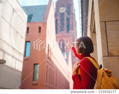 Tourist woman strolls through old town of Frankfurt, exploring its historic streets, beautiful architecture, and cultural landmarks, enjoying vibrant atmosphere of citys past. 133936277