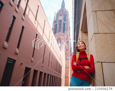 Tourist woman strolls through old town of Frankfurt, exploring its historic streets, beautiful architecture, and cultural landmarks, enjoying vibrant atmosphere of citys past. 133936279