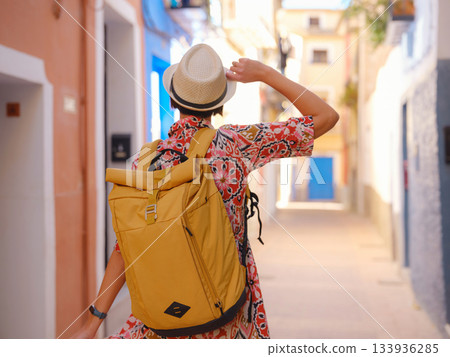 Woman in dress strolls through colorful streets of Spanish coastal town of La Vila Joiosa . sunny winter atmosphere highlights charm of Mediterranean architecture and quiet seaside life, back view 133936285