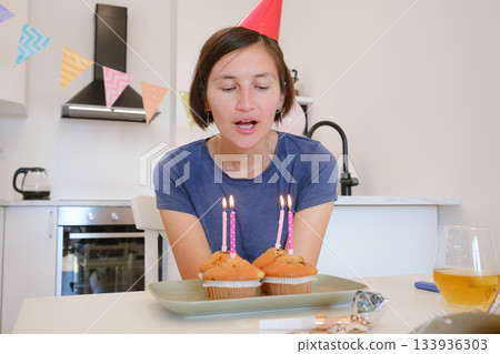 Woman celebrates with four cupcakes topped with candles in place of traditional birthday cake. Smiling and joyful, he enjoys cozy and unique celebration, creating warm and memorable festive moment. Woman celebrates with four cupcakes topped with candles in place of traditional birthday cake. Smiling and joyful, he enjoys cozy and unique celebration, creating warm and memorable festive moment. 133936303