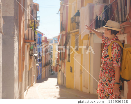 Woman in dress strolls through colorful streets of Spanish coastal town of La Vila Joiosa or Villajoyosa. sunny winter atmosphere highlights charm of Mediterranean architecture and quiet seaside life 133936318