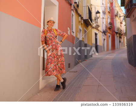 Woman in dress strolls through colorful streets of Spanish coastal town of La Vila Joiosa or Villajoyosa. sunny winter atmosphere highlights charm of Mediterranean architecture and quiet seaside life 133936319