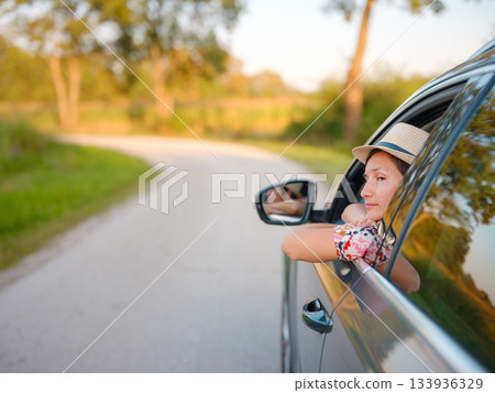 Traveler woman in red ethnic dress and hat drives car through scenic countryside of Croatia in summer. Surrounded by lush fields and forests, she enjoys peaceful and adventurous road trip Traveler woman in red ethnic dress and hat drives car through scenic countryside of Croatia in summer. Surrounded by lush fields and forests, she enjoys peaceful and adventurous road trip 133936329