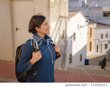 Young woman strolling through charming narrow streets of Denia, Alicante province, Spain, surrounded by historic Mediterranean architecture , enjoying peaceful atmosphere and cultural ambiance. 133936331