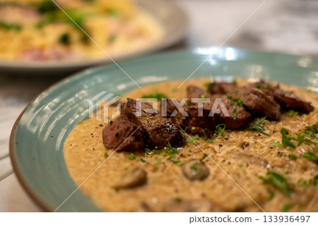 Risotto with sliced meat steak served on plate. It is a popular Italian rice dish. 133936497