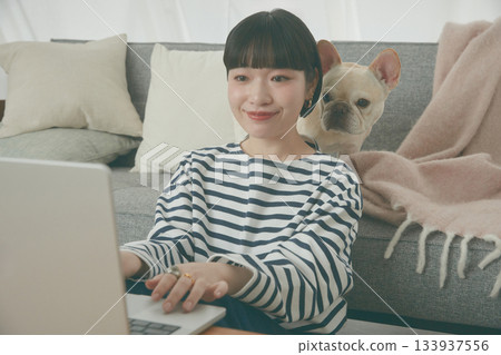 一位女士正在電腦前工作,一隻狗在一旁看著她。 一位女士正在電腦前工作,一隻狗在一旁看著她。 133937556