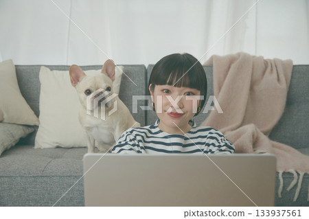 一位女士正在電腦前工作，一隻狗在一旁看著她。 133937561