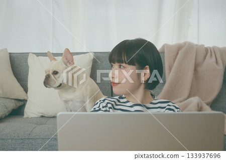 一名女子正在使用電腦，旁邊還有一隻狗。 133937696
