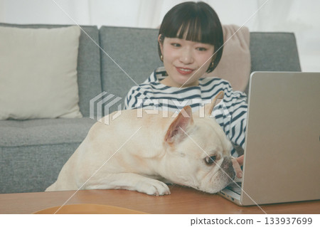 一位女士正在電腦前工作，一隻狗在一旁看著她。 133937699