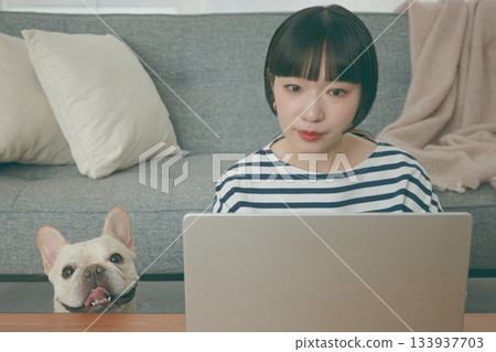 一位女士正在電腦前工作，一隻狗在一旁看著她。 133937703