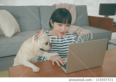 一位女士正在電腦前工作，一隻狗在一旁看著她。 133937721