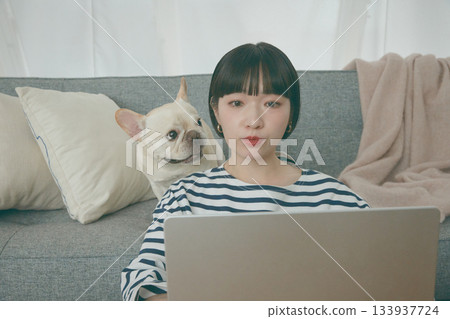 一位女士正在電腦前工作，一隻狗在一旁看著她。 133937724