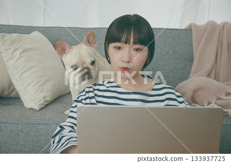 一位女士正在電腦前工作，一隻狗在一旁看著她。 133937725