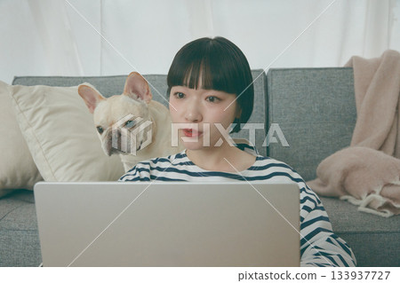 一位女士正在電腦前工作，一隻狗在一旁看著她。 133937727