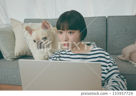 一位女士正在電腦前工作，一隻狗在一旁看著她。 133937729