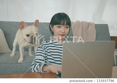 一位女士正在電腦前工作，一隻狗在一旁看著她。 133937796