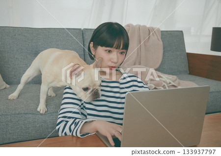 一位女士正在電腦前工作,一隻狗在一旁看著她。 一位女士正在電腦前工作,一隻狗在一旁看著她。 133937797