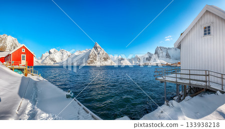 Traditional Norwegian  houses on the shore of  Reinefjorden on Toppoya island and snowy mountaines in background 133938218