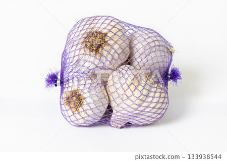 Garlic bulbs in purple mesh packaging bag isolated on white background 133938544