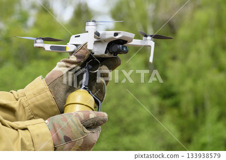 Operator in military colored clothes Preparing a drone for flight attached grenade 133938579