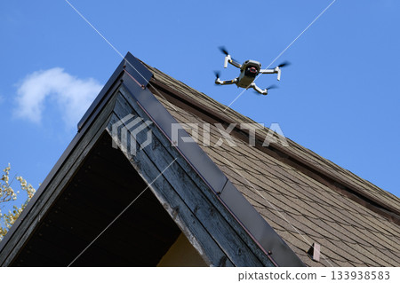 Drone in the air inspecting the roof over the house closeup blue sky 133938583