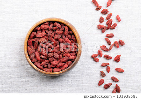 Dried goji berries, in a wooden bowl on linen. Also known as Chinese wolfberry, red medlar, and matrimony vine. Bright orange-red sweet fruits of Lycium barbarum native to China and across Asia. Photo 133938585