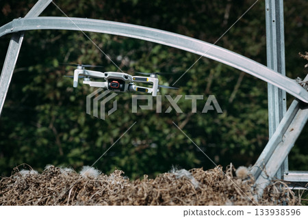 Small Flying Quadcopter Drone in flight mode with camera pointed at viewer outdoor destroyed rebar frame green background 133938596