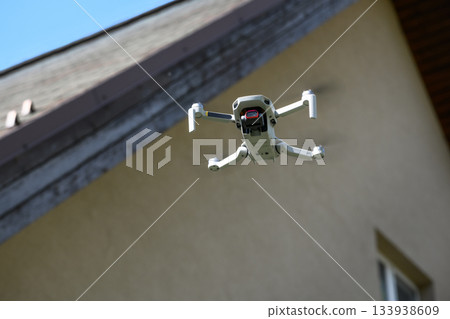 Drone in the air inspecting the roof over the house closeup blue sky background Drone in the air inspecting the roof over the house closeup blue sky background 133938609