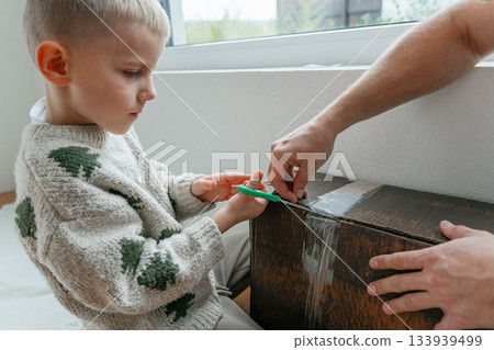 A young child helps an adult open a vintage wooden box near a bright window. The moment captures curiosity, learning and warm interaction in a cozy home environment. Perfect for family, childhood and A young child helps an adult open a vintage wooden box near a bright window. The moment captures curiosity, learning and warm interaction in a cozy home environment. Perfect for family, childhood and 133939499
