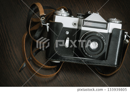 The Classic Vintage Old shabby Photo Camera in a black case open lens brown natural leather Strap on  Wooden table 133939805