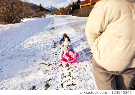 Family fun in the snow with children sledding down hill in Winter on snowy day 133940345