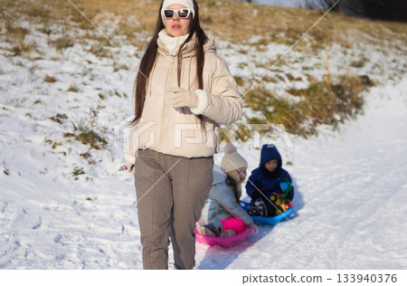 Woman walks near children sledding on snow covered hill during Winter in daytime 133940376