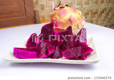 Sliced vibrant dragon fruit on white plate with whole fruit 133940579