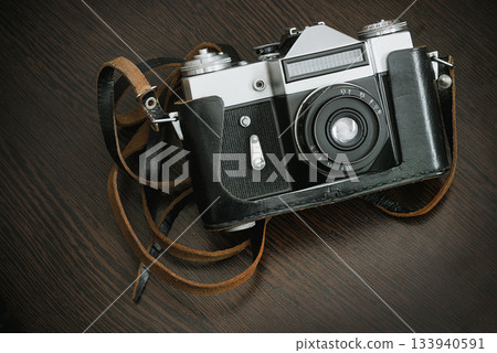 The Classic Vintage Old shabby Photo Camera in a black case open lens brown natural leather Strap on Wooden table The Classic Vintage Old shabby Photo Camera in a black case open lens brown natural leather Strap on Wooden table 133940591