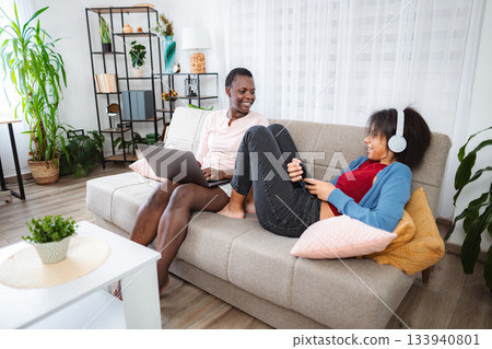 Mother and Daughter Relaxing on Sofa, Using Laptop and Listening to Music Mother and Daughter Relaxing on Sofa, Using Laptop and Listening to Music 133940801