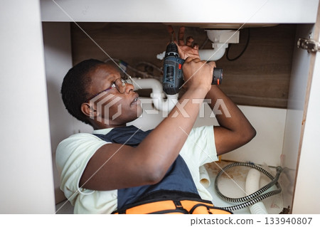 Plumber Lying Down and Repairing Sink Pipes with a Drill Plumber Lying Down and Repairing Sink Pipes with a Drill 133940807