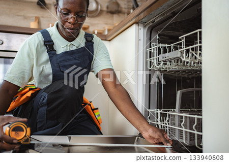 Technician taking measurements for dishwasher installation in kitchen Technician taking measurements for dishwasher installation in kitchen 133940808