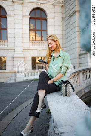 Woman sitting on street in Vienna using smartphone 133940824
