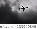 Large passenger airplane airliner silhouette flying in the cloudy sky bottom view dark grey clouds 133940849
