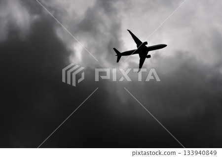 Large passenger airplane airliner silhouette flying in the cloudy sky bottom view dark grey clouds Large passenger airplane airliner silhouette flying in the cloudy sky bottom view dark grey clouds 133940849