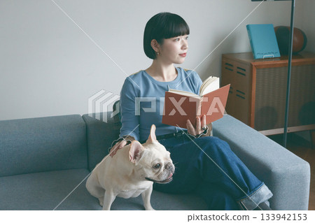 一位年輕女子和一隻狗在沙發上放鬆休息。 一位年輕女子和一隻狗在沙發上放鬆休息。 133942153