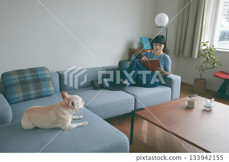 一位年輕女子和一隻狗在沙發上放鬆休息。 133942155