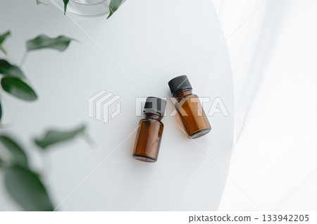 棕色的精油瓶和幾盆綠植整齊地擺放在一張白桌上，營造出一種自然簡約的氛圍。 133942205